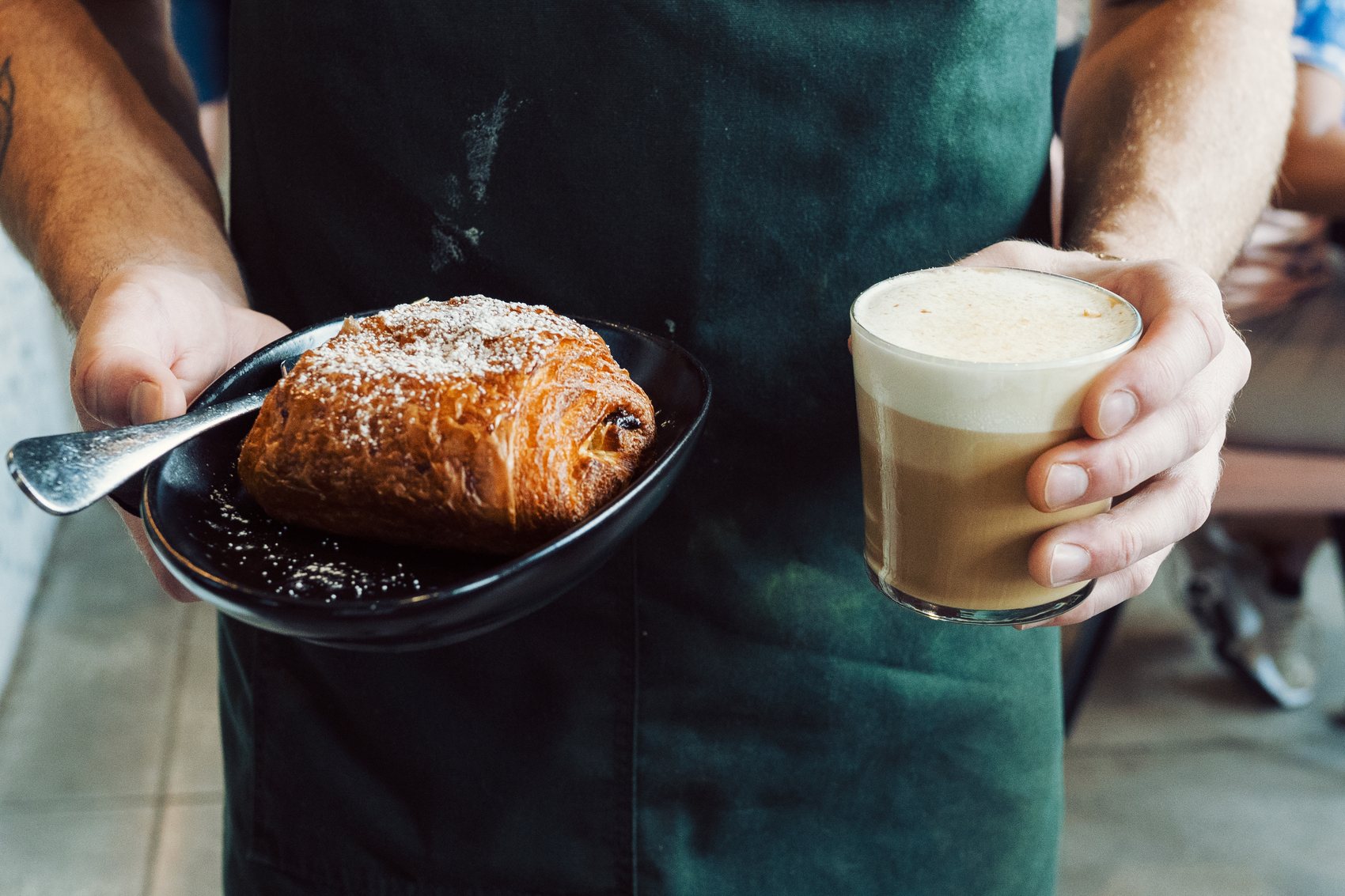A barista presenting a croissant and latte at Stemma Craft Coffee